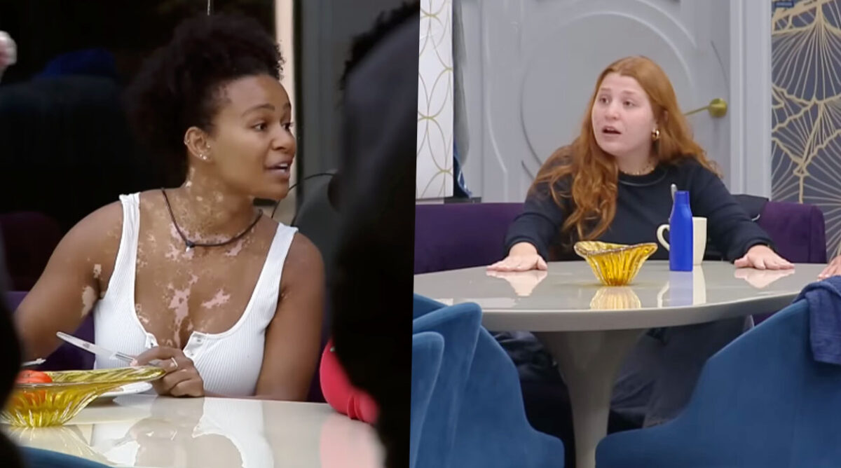 Natália discute com Giulia em A Grande Conquista. Ex-BBB usa camiseta branca e segura par de talheres, enquanto Giulia coloca as palmas das mãos sobre a mesa e usa um casaco preto.