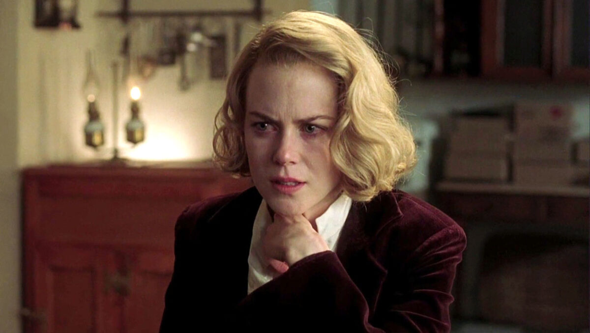 Nicole Kidman usando camiseta social branca e casaco vinho enquanto coloca a mão no pescoço em cena de Os Outros, terror que retornou ao catálogo da Prime Video.
